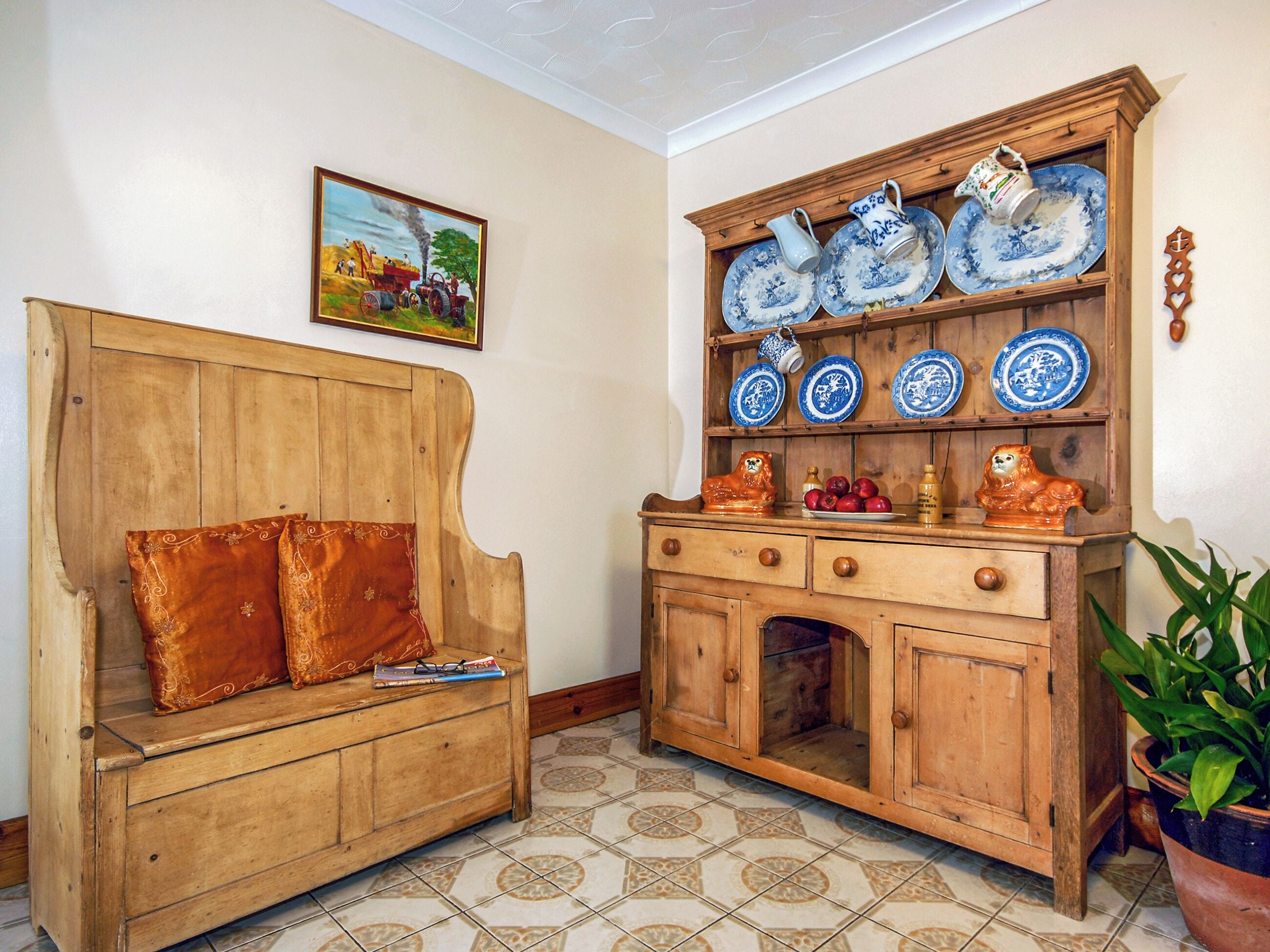 Une pièce comprenant un banc en bois, un buffet avec des assiettes bleues et blanches, et un tableau accroché au mur.