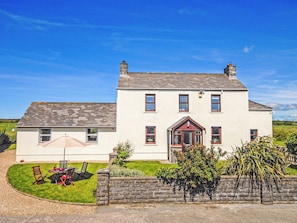 A two-story house with a front porch, a small garden with chairs, and a stone wall.