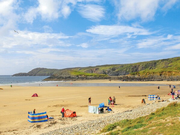 A beach with tents, a rocky shoreline, and a hilly landscape in the background.