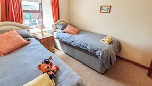 Une chambre d’hôtel avec deux lits, une table de chevet, une lampe et un ours en peluche sur l’un des lits.