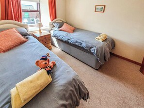 A hotel room with two beds, a nightstand, a lamp, and a teddy bear on one bed.
