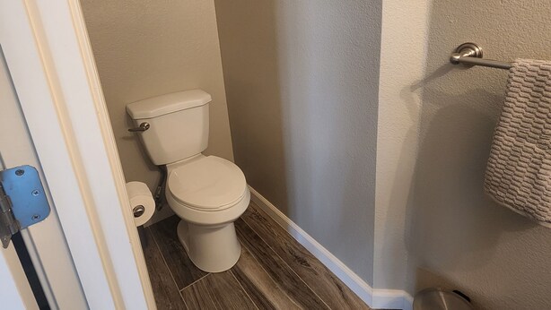 A bathroom with a toilet, a trash can, and a towel rack.