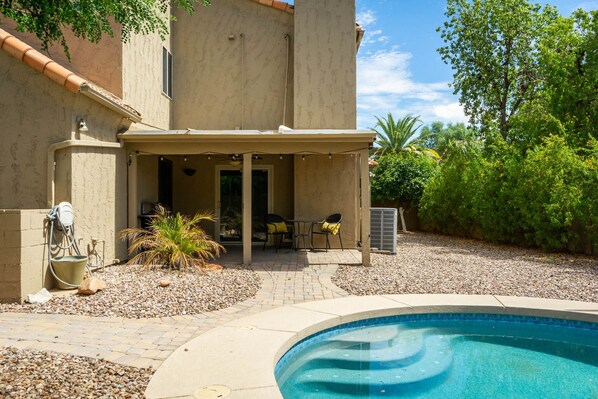 A backyard with a swimming pool, patio seating, and a covered area with a hose. - Luxury Updated 3-bedroom home with pool in Gilbert (Gilbert)