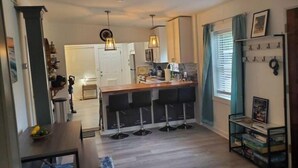 Una cocina moderna con una isla central, taburetes de bar, iluminación colgante y un comedor con mesa y sillas.