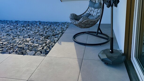 A patio with a hanging chair and umbrella, a tiled floor, and a view of houses in the background.