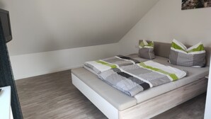A modern, minimalist bedroom with a sloped ceiling, a bed with a striped and geometric-patterned bedspread, and two pillows with green accents.
