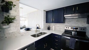 A modern kitchen with dark cabinets, a white countertop, stainless steel appliances, and a built-in dishwasher.