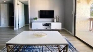 A modern living room with a white entertainment unit, a flat-screen TV, and a coffee table.