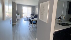 A modern kitchen with a built-in dishwasher, a dining area with a table and chairs, and a living room with a sofa and a TV.