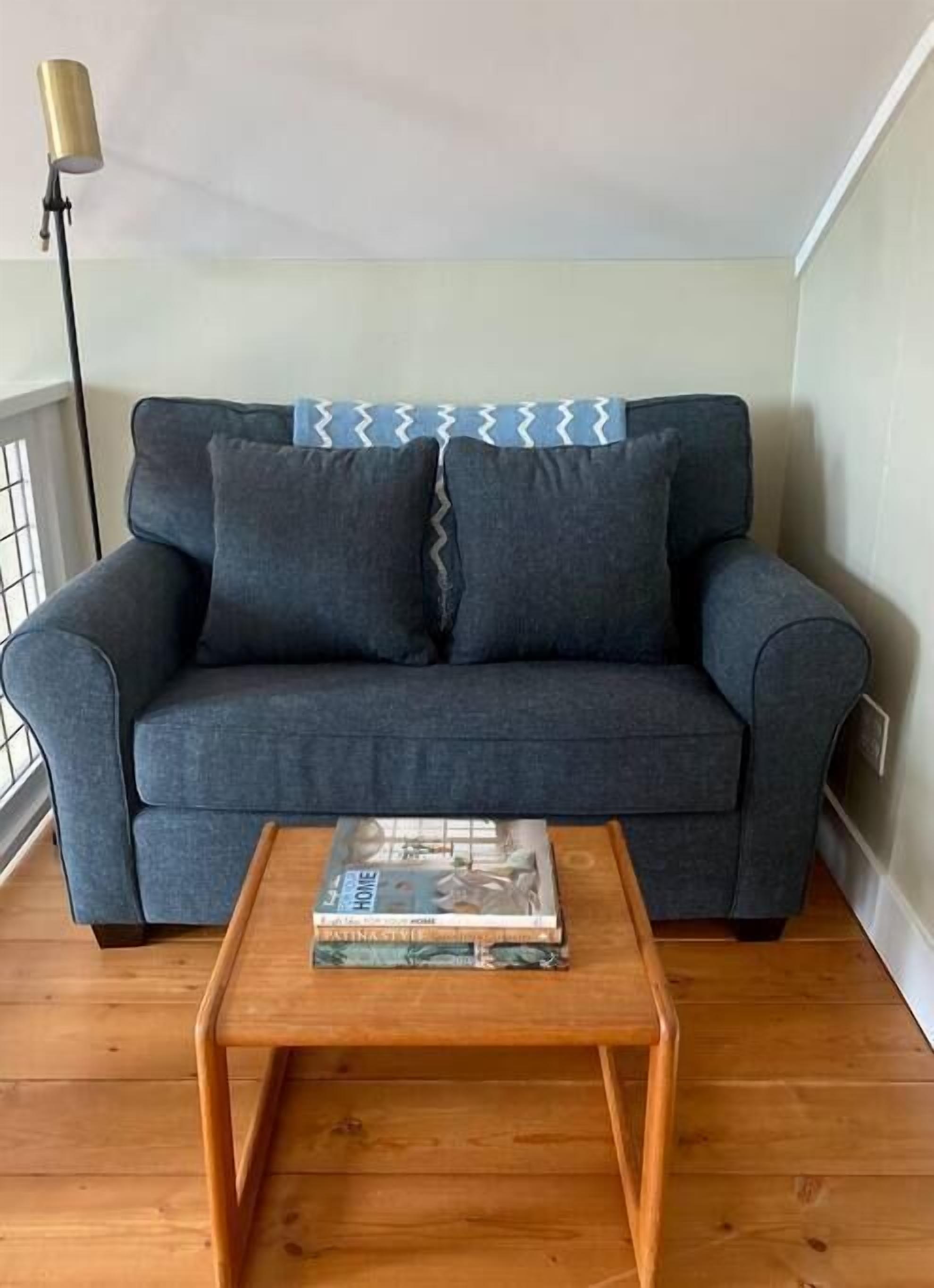 Ein graues Sofa mit einem gemusterten Überwurf, ein Holztisch mit einer Zeitschrift und eine Stehlampe.