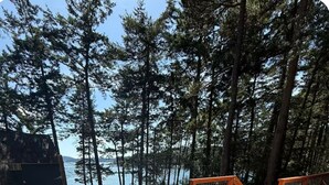 Een hottub op een houten terras met uitzicht op een bos en een wateroppervlak.