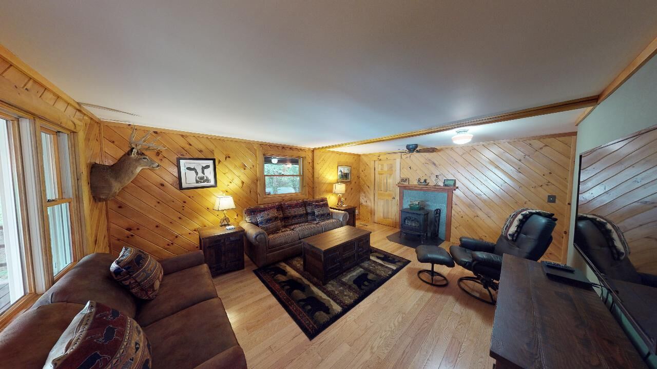 Un salon chaleureux avec des murs en bois, un canapé, une table basse, une cheminée et une tête de cerf accrochée au mur.