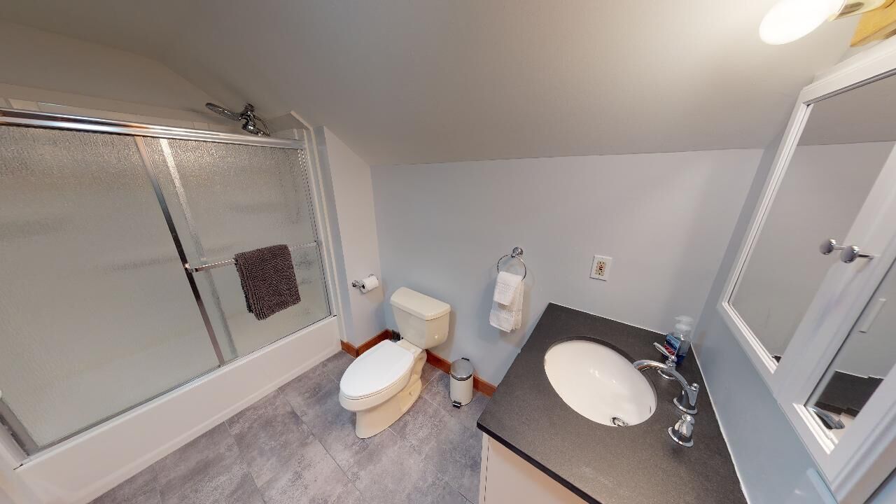 Ein Badezimmer mit Duschkabine aus Glas, Toilette, Waschbecken und Spiegel.