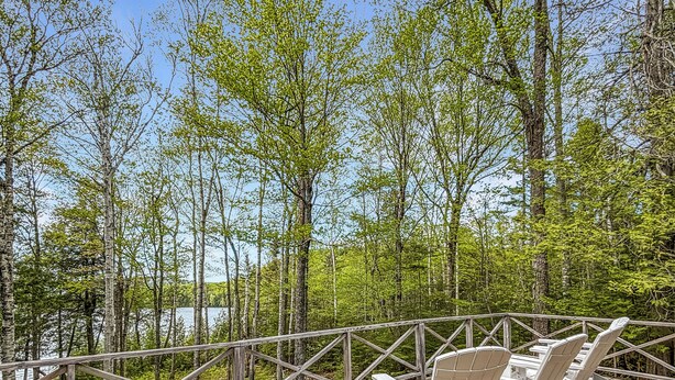 Ett trädäck med Adirondack-stolar med utsikt över ett skogsområde och en sjö eller ett annat vattendrag.