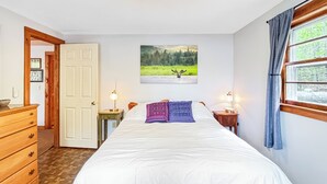 Ett sovrum med en säng, två sänglampor, en tavla som föreställer en älg, en byrå i trä och en dörr.
