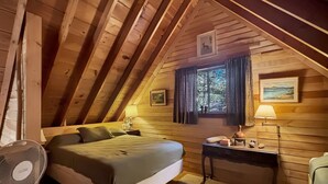 A cozy attic bedroom with a bed, a bedside table, a lamp, and a window with curtains. - Horizons West Hideaway (Waterfront on Moosehead Lake) (Greenville)