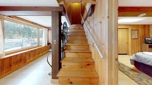 Eine Holztreppe in einer Hütte mit Blick auf eine verschneite Landschaft durch große Fenster.