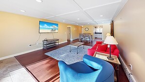 A spacious living room with a blue armchair, a red sofa, and a dining area with a table and chairs. - Lakeside Loft (Direct Access to Moosehead Lake!) (Greenville)