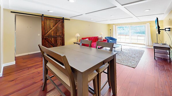 A spacious room with a wooden dining table, red and blue chairs, a red sofa, and a large window with a view.