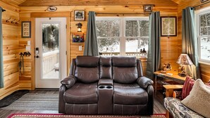 Ein gemütliches Blockhaus-Interieur mit einem Ledersessel, Holzwänden, einem großen Fenster mit Blick auf Schnee und einer Tür mit Glasfenster.