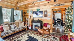Ein gemütliches Blockhaus-Interieur mit Kamin, Holzwänden, einer Couch und einem Weihnachtsbaum.