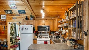 Eine gemütliche Küchenzeile im Chalet-Stil mit Holzschränken, einem weißen Kühlschrank, einer Mikrowelle und einem Herd.