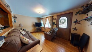A cozy living room with a brown sofa, a television, and a wooden floor. - Tranquil Times (In Town with Direct ATV/Snowmobile Access!) (Greenville)