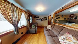 A cozy living room with a wooden floor, a brown sofa, a recliner, and a large mirror. - Tranquil Times (In Town with Direct ATV/Snowmobile Access!) (Greenville)