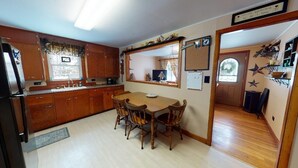 A kitchen with wooden cabinets, a dining table with chairs, a refrigerator, and a window with curtains. - Tranquil Times (In Town with Direct ATV/Snowmobile Access!) (Greenville)