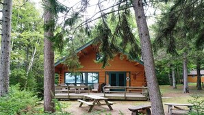 Une cabane dotée d’une véranda, de tables de pique-nique et entourée d’une forêt.