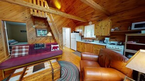 A cozy cabin interior with a loft bedroom, a kitchenette, and a living area with a sofa and a chair. - Stony Cove Camp (Waterfront on Lower Wilson Pond!) (Greenville)