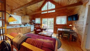 A cabin interior with a wooden ceiling, a sofa, a dining table, a TV, and a kitchen area. - Stony Cove Camp (Waterfront on Lower Wilson Pond!) (Greenville)