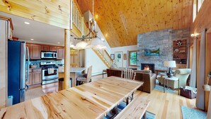 Un'ampia cucina con elettrodomestici moderni, un'area pranzo con un lungo tavolo in legno e un accogliente soggiorno con camino.