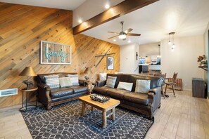 Ein modernes Wohnzimmer mit einer Wand als Holzdekor, einem Deckenventilator und einer Küche im Hintergrund.