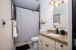 Un bagno con tenda da doccia a righe, un water bianco, un lavabo con piano in granito e uno specchio con un cartello che dice 'Love'.