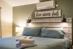 A bedroom with a bed, pillows, a wall-mounted air conditioner, and a motivational quote sign.