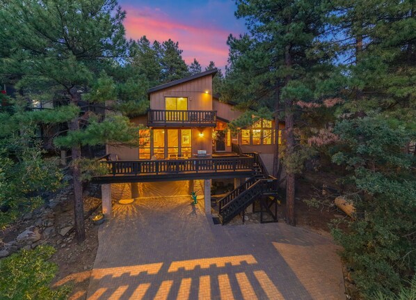 A two-story lodge with a balcony, surrounded by trees, and featuring a paved driveway.