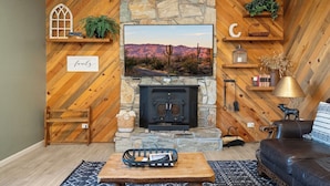 A cozy living room with a stone fireplace, wooden shelves, and a comfortable seating area. - Cozy Munds Park Cabin ~ Fire Pit & Sunset Views (Munds Park)