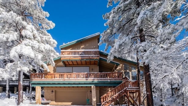 A two-story building with a balcony, surrounded by snow-covered trees. - Cozy Munds Park Cabin ~ Fire Pit & Sunset Views (Munds Park)