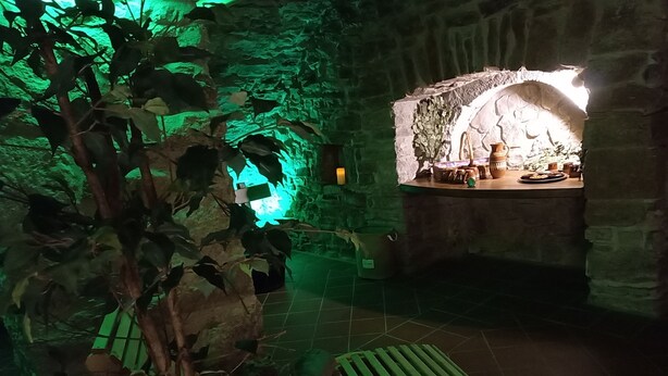 Un interior tenuemente iluminado, con una pared de piedra, una planta iluminada en verde y un banco.