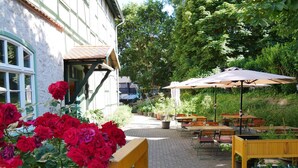 An outdoor patio area with wooden tables and chairs, surrounded by potted plants and a yellow fence. - Schloss Goldacker - das Schloss der Gesundheit (Unstrut-Hainich)