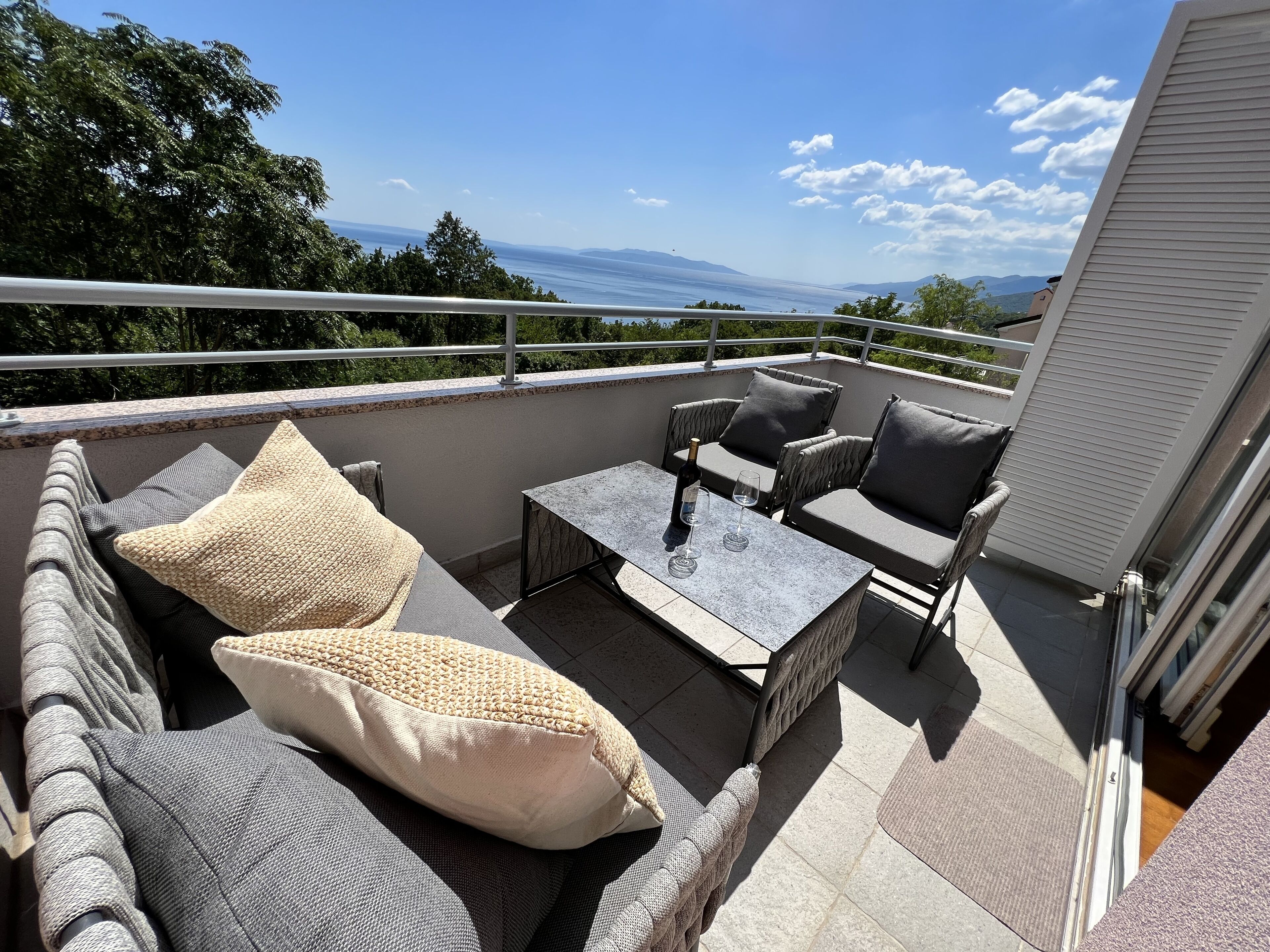 Un balcon avec des meubles d’extérieur, une table et une bouteille de vin.