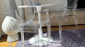 Ein Zimmer mit einem klaren Glastisch, Stühlen, einer blauen Lampe und einem violetten Teppich mit Muster.