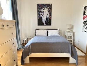 Une chambre à coucher avec un lit, une commode, une table de chevet et un tableau accroché au mur.
