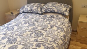A bed with a blue and white patterned bedspread, a grey headboard, and wooden nightstands with drawers. - London Luxury 1 bed flat - kitchen, garden, parking, WIFI (Ilford)