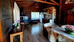 Interior acogedor de una cabaña de madera con comedor, cocina y un gran techo con estructura de madera.
