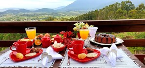 Ein Tisch ist reichhaltig mit Frühstücksleckereien gedeckt, darunter Gebäck, Früchte und Kuchen, mit Blick auf eine reizvolle Landschaft.