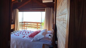 Dormitorio de cabaña de madera con cama, mesita de noche y vistas al exterior.