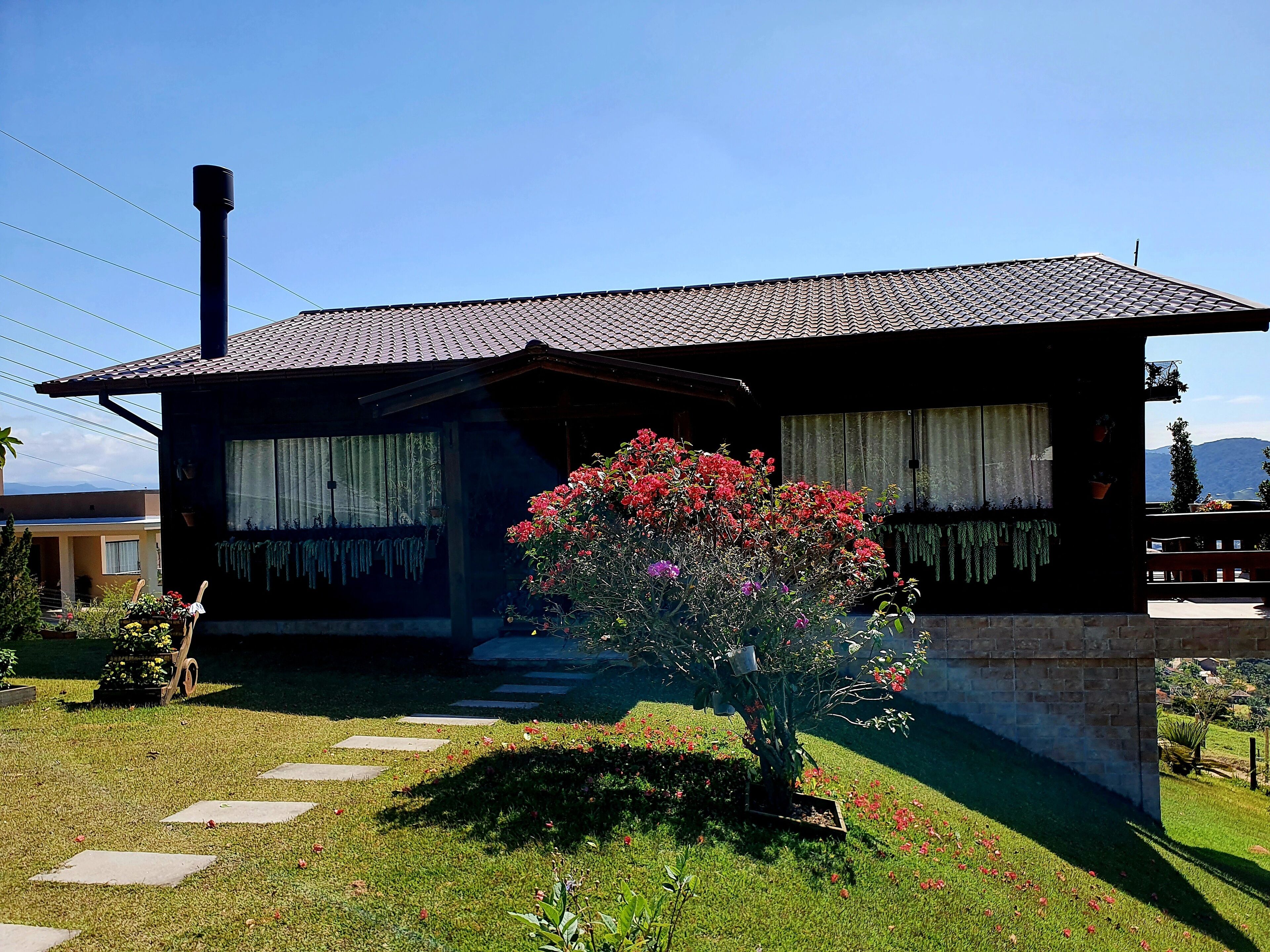 A traditional house with a tiled roof, a chimney, and a garden with a flowering bush.