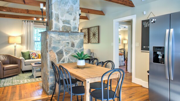 A dining area with a stone fireplace, wooden ceiling beams, and a modern refrigerator. - Firefly Cottage | Pet-Friendly, Fire Pit, 8 Mins to DT AVL + Biltmore Pass (Asheville)